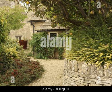 Englisches Cotswold Steinhaus mit traditioneller Architektur, eingebettet in einen üppigen Garten mit einem gewundenen Kiesweg und einer Steinmauer. Cotswolds, England, Stockfoto