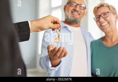 Immobilienmakler überreicht Hausschlüssel an lächelndes reifes Paar während der Schließung Stockfoto