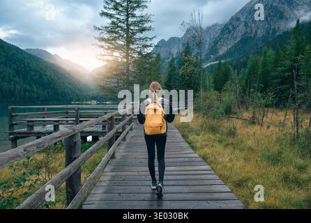 Frau mit gelbem Rucksack, die auf einem Holzweg am alpinen lak läuft Stockfoto