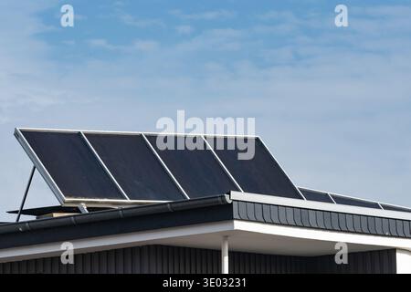 Solarpaneele werden auf dem Dach eines Hauses installiert. Der Himmel ist klar mit ein paar Wolken. Das Haus hat ein schlichtes Design und die Paneele zeigen der Sonne bis zur Farbe Stockfoto