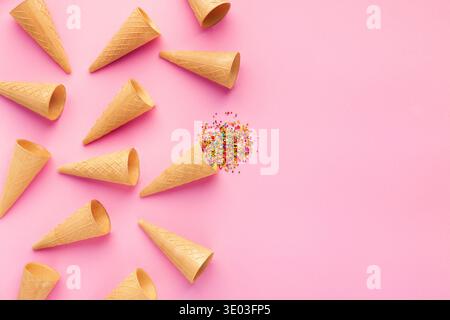 Leere Eiswaffelkegel und bunte Streusel auf rosa Hintergrund, Stockfoto