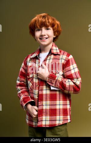 Ein fröhliches Kind mit leuchtend roten Haaren zeigt einen modischen Look in einem karierten Hemd. Stockfoto
