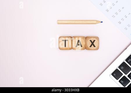 Draufsicht auf Holzblöcke, die das Wort TAX auf einer hellen neutralen Oberfläche mit einer Ecke eines Laptops, einem Bleistift und einem Kalender buchstabieren. Stockfoto