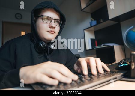 Ein Teenager-Hacker oder Programmierer arbeitet intensiv an seinem Computer und gibt in einem dunklen Raum Code ein. Stockfoto