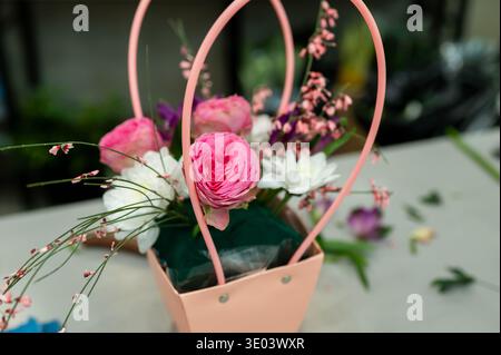 Nahaufnahme eines wunderschönen Blumenstraußes mit rosa Ranunkeln und weißen Chrysanthemen in einer pinkfarbenen Papiertüte mit Griffen an einem Arbeitsplatz in einer Blume Stockfoto