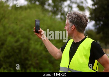 Seitenansicht eines männlichen Radfahrers mit reflektierender Sicherheitsweste mit Smartphone während einer Radtour auf dem Land. Stockfoto