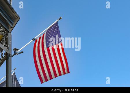Die Nationalflagge der Vereinigten Staaten von Amerika, die Sterne und Streifen, die von einem Gebäude vor einem tiefblauen Himmel fliegen. Keine Personen. Stockfoto
