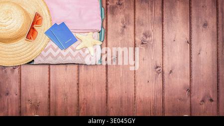 Auf Holzoberfläche sind die Grundausstattung für den Sommer am Strand angeordnet, einschließlich Strohhut, Sonnenbrille, Handtücher, Seesterne und blauem Reisepass Stockfoto