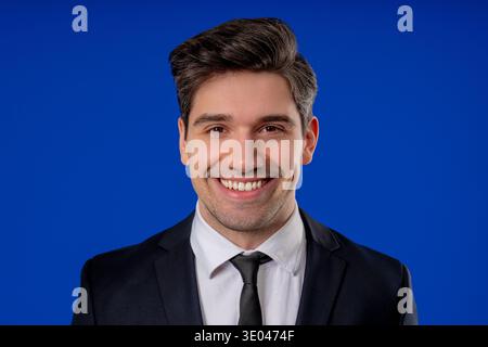 Porträt des glücklichen Geschäftsmannes, der auf blauem Studiohintergrund lächelt. Mann im Business-Anzug, der in die Kamera schaut. Freundlicher, gutaussehender Kerl. Stockfoto
