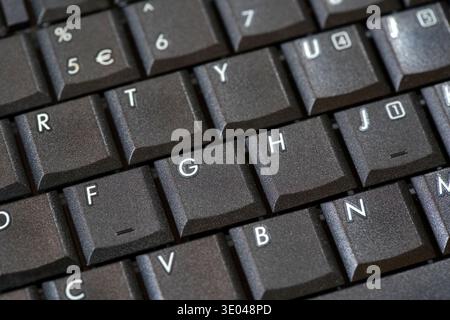 Schwarze Laptoptastatur mit Makrodetail, abgewinkelte Nahaufnahme strukturierter Tastenkappen mit Buchstaben und Zahlenzeile, Hintergrund für Computereingabe im Büro Stockfoto
