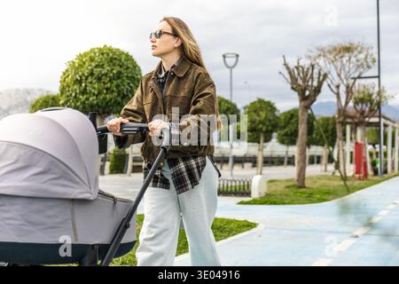 Eine Mutter macht einen gemütlichen Spaziergang durch den Park und schiebt ihr Baby in einen Kinderwagen. Die ruhige Umgebung und das Grün sorgen für einen entspannenden Outdoor-Aufenthalt Stockfoto