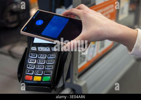 Hand mit Smartphone für kontaktlose Ladenzahlungen. Nahaufnahme eines Kunden, der ein Smartphone an einem Kartenterminal antippt, um eine schnelle kontaktlose Zahlung bei einem zu ermöglichen Stockfoto