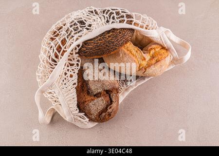 Eine Auswahl an frisch gebackenen Vollkornbroten in einem wiederverwendbaren Netzbeutel mit verschiedenen Texturen und Krusten, die auf einem neutralen B präsentiert werden Stockfoto