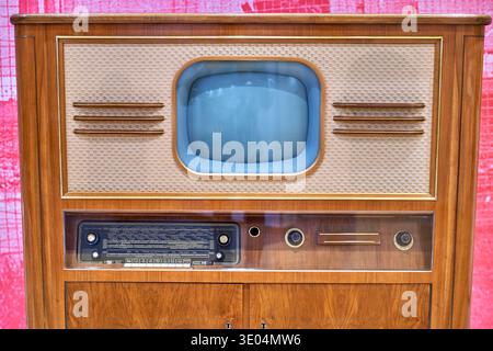 Ein Vintage-TV- und Radio-Kombi aus Holz aus der Mitte des 20. Jahrhunderts, vor einem rosa gemusterten Hintergrund. Das Gerät... Stockfoto