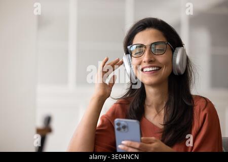 Lächelnde Latina-Frau in Brille, die Musik über Kopfhörer genießt Stockfoto