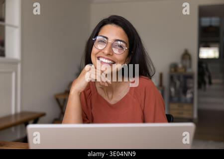 Junge, fröhliche Frau in Brille sitzt am Schreibtisch mit Laptop Stockfoto