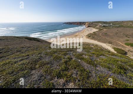 Aus der Vogelperspektive auf eine abgelegene Küstenlandschaft mit goldenem Sand, sanften Wellen und zerklüfteten Klippen in der Algarve. Stockfoto