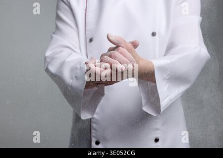 Profi-Chefkoch mit Mehl an den Händen vor grauem Hintergrund, Nahaufnahme Stockfoto