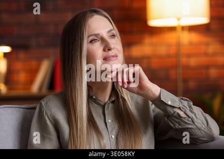 Nachdenkliche Frau, die zu Hause auf einem Sessel ruht Stockfoto
