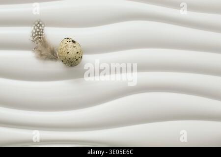 Kreatives Osterkonzept mit Quall-Ei auf weicher Feder auf moderner welliger weißer Oberfläche. Minimales saisonales Stillleben mit Kopierraum. Stockfoto
