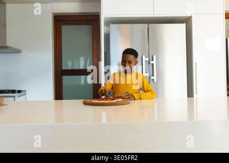 Afroamerikanisches Kind, das gelbe Spreizsoße auf Pizzateig in der Küche trägt, Schüssel hält, Löffel. Kind, zu Hause, kochen, Tomate, hell, modern, minim Stockfoto