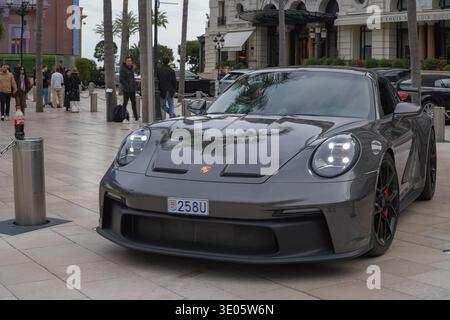Porsche 911 GT3 fährt durch den Place du Casino, Monaco. Luxusautos, Fußgänger und großartige Architektur des Monte Carlo Casino-Viertels sichtbar. Stockfoto