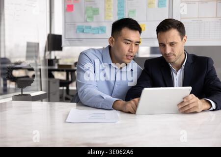 Junger Geschäftsmann präsentiert Daten auf Tablette vor älteren männlichen Kollegen Stockfoto