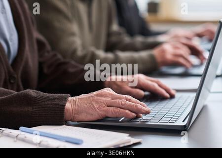 Anonyme Frau, die während des Computerkurses auf dem Laptop schreibt, mit anderen Erwachsenen im Klassenzimmer sitzt, mit der Tastatur anspricht, an der Schulung zu digitalen Fähigkeiten teilnimmt Stockfoto