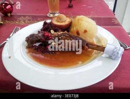 Gebratene Schweinshaxe Mit Soße, Geschmorter Rotkohl Und Kartoffelknödel Auf Weißer Platte, Knusprige Haut In Reichhaltiger Sauce Glasiert, Knochen In Folie Gewickelt, Falten Stockfoto
