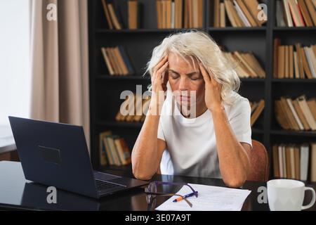 Kopfschmerzen. Frau mittleren Alters, die Schläfe berührt und Stress erlebt. Reife alte Dame müde der Arbeit, Kopfschmerzen krank, die Schläfen an der Stirn reibt. Long-Laptop-Nutzung Computer Vision Office Syndrom Stockfoto