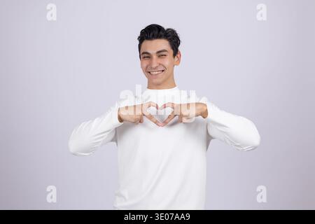 Mann in weißem Pullover, der Herzzeichen mit Fingern macht Stockfoto