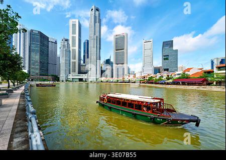 Gruppen von Menschen machen an einem sonnigen Tag eine Bootsfahrt entlang des Flusses in der Innenstadt von Singapur, umgeben von hohen Gebäuden. Stockfoto