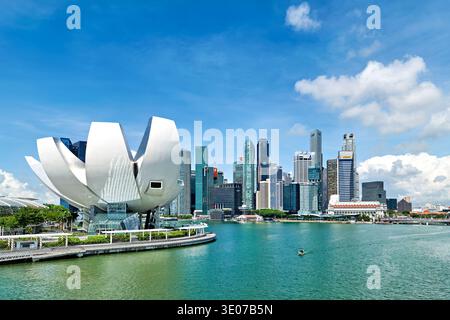 Die Menschen schauen sich das ArtScience Museum in der Nähe des Wassers an, während die Skyline der Stadt an klaren Tagen im Hintergrund zu sehen ist. Stockfoto