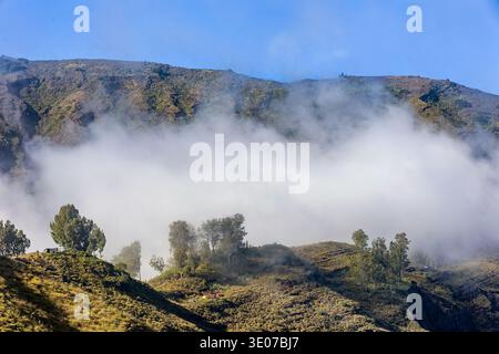 Dramatische Bergtallandschaft, die teilweise von dickem Nebel unter einem klaren blauen Himmel verdeckt wird Stockfoto