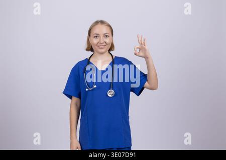 Lächelnde Krankenschwester in blauer Uniform mit OK-Zeichen Stockfoto