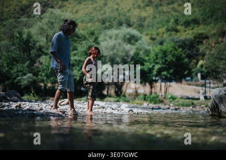 Zwei Freunde spazieren an einem Sommerufer entlang und waten barfuß in einer ruhigen, natürlichen Umgebung Stockfoto