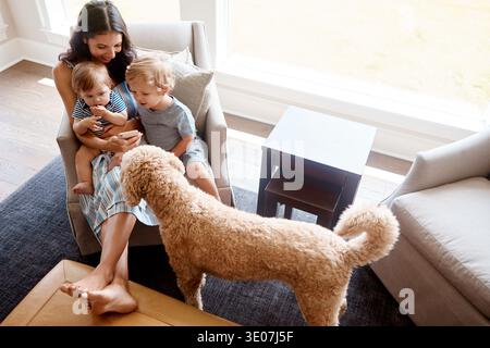 Hund, Kinder und Mutter mit Telefon auf dem Sofa zum Streamen von Zeichentrickfilmen, Verbundenheit oder glückliche Familie. Haustier, Kinder und Mutter mit Smartphone zu Hause für Stockfoto