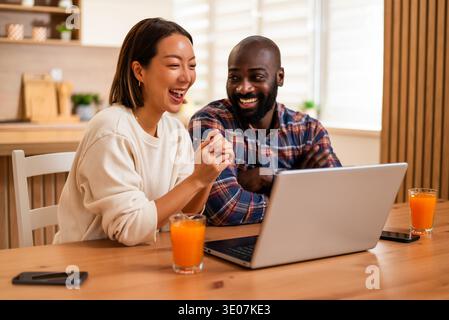 Fröhliches erwachsenes Paar sitzt zusammen an einem Holztisch und benutzt Laptop für Videokommunikation. Stockfoto