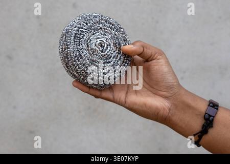 Nahaufnahme einer weiblichen Hand, die einen Schwamm aus Edelstahl zum Reinigen von Geschirr hält. Ein praktisches Küchenutensil für die Housekeeping, Washin Stockfoto
