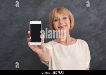 Lächelnde reife Frau, die ein Smartphone mit leerem Bildschirm hält Stockfoto