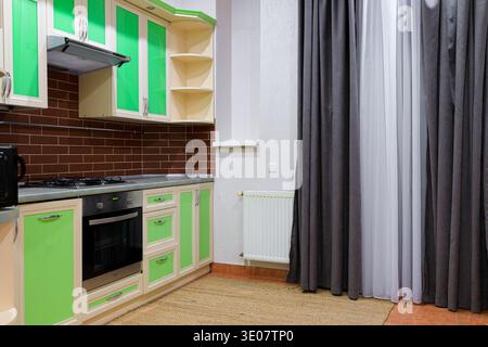 Die moderne Küche verfügt über leuchtend grüne Schränke, einen Gasherd, einen Backofen und einen strukturierten Backsteinboden Stockfoto