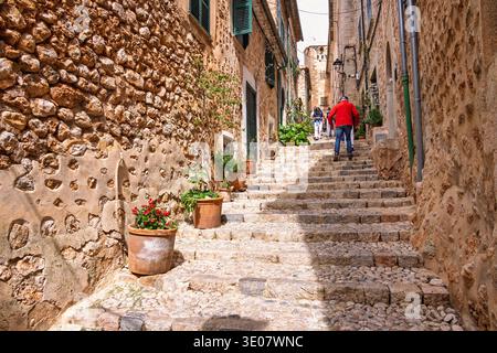 Touristen wandern auf einer kopfsteingepflasterten Treppe mit Zierpflanzen an der Hausmauer im alten malerischen Dorf Fornalutx auf Mallorca Stockfoto