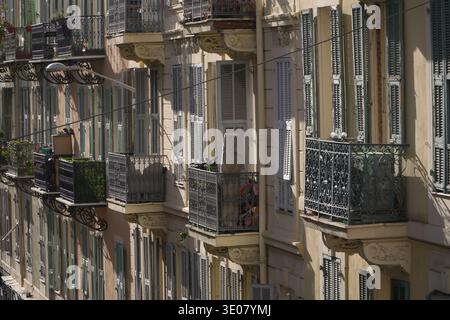 Wohnfassade mit kunstvollen schmiedeeisernen Balkonen und geschlossenen hellblauen Lamellen an der Außenfassade des Gebäudes in Nizza, Frankreich. Stockfoto