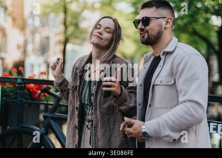 Junges Paar genießt eine sonnige Amsterdamer Kanalbrücke, während es Musik hört und ein Telefon benutzt Stockfoto
