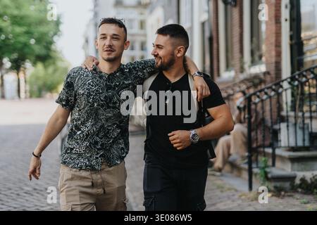 Zwei Freunde, die Arm in Arm durch die Straßen Amsterdams gehen an einem sonnigen, ungezwungenen Tag Stockfoto
