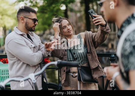 Junge Freunde machen ein Selfie an einem Kanal in Amsterdam, während sie mit Fahrrädern stehen und sich unterhalten Stockfoto