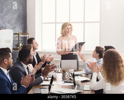 Lächelnde Chefin und Team klatschen bei der Besprechung die Hände Stockfoto