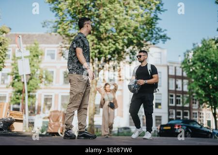 Zwei Freunde unterhalten sich auf einer sonnigen Straße in den Niederlanden mit legeren Rucksäcken und Sonnenbrillen Stockfoto