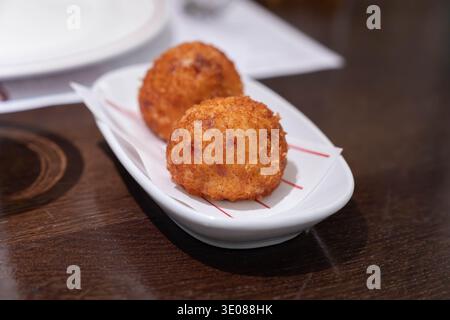 Goldene knusprige gebratene Snackbällchen, serviert auf einer kleinen Keramikplatte in einem Restaurant mit knuspriger Textur und warmen frisch zubereiteten Komfortgerichten Stockfoto