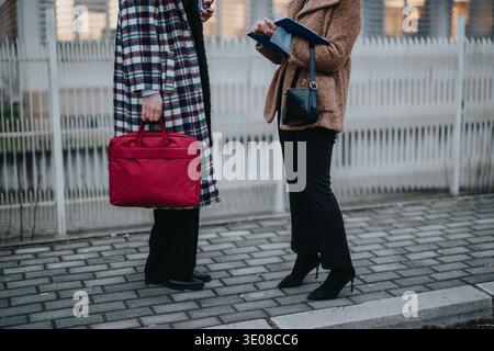 Zwei Profi-Frauen diskutieren im Freien Dokumente, mit roter Tasche und Klemmbrett, elegant gekleidet Stockfoto